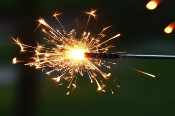 Obraz premium Festive sparkler emitting bright sparks against a blurred green background creating a celebratory mood for holiday events and summer nights