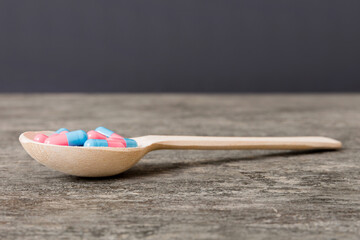 Vitamin capsules in a spoon on a colored background. Pills served as a healthy meal. Red soft gel vitamin supplement capsules on spoon