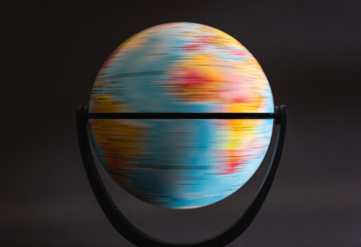 Colorful toy globe spinning rapidly against a dark background. The motion blur emphasizes the rotation of the miniature Earth model, creating a dynamic sense of movement and energy