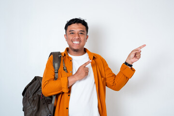 Image of handsome young Asian student using backpack with hand pointing to left side on isolated...