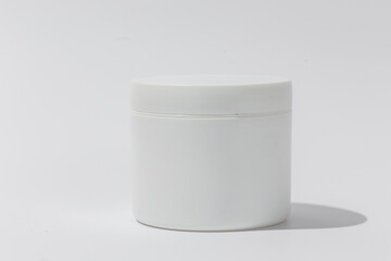 White Cosmetic Cream Jar. Cylinder on textured tan paper with shadows