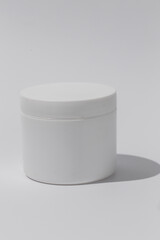 White Cosmetic Cream Jar. Cylinder on textured tan paper with shadows