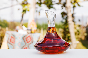 Wine decanter with rich rose wine on a table set against a vineyard backdrop.
