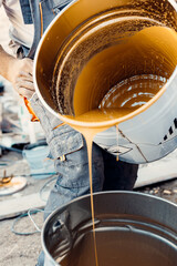 Construction worker pouring epoxy resin from metal bucket into another bucket