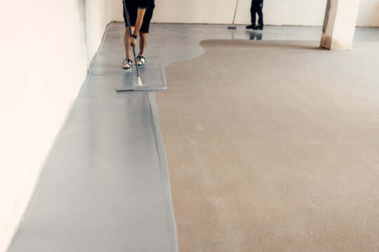 Construction workers applying epoxy resin flooring in industrial building