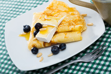 Homemade breakfast sweet crepes with honey, brie, blueberries and pine nuts