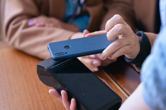 Close-up elderly couple wearing sunglasses and casual outfits, sitting at a table and sharing a joyful moment while using a smartphone. Natural lighting and warm expressions in outdoor setting. 