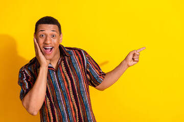 Smiling young man making a surprised expression and gesturing on a bright yellow background wearing...