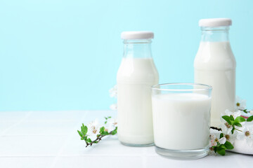 Fresh milk and blossoms on white table against light blue background. Space for text