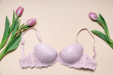 Pink lace bra and tulip flowers on beige background, flat lay