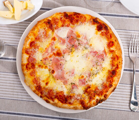 Delicious pizza with crispy sides, cheese and prosciutto. Serving hot pizza just from the oven on the table. Italian pizza for lunch
