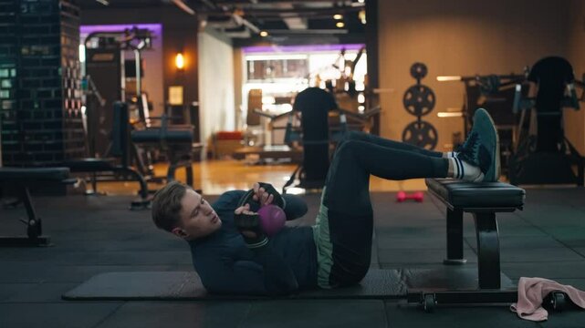 Man Doing Twisted Crunches with Kettlebell Exercise for the Abs and Obliques in Modern Gym - static slow motion
