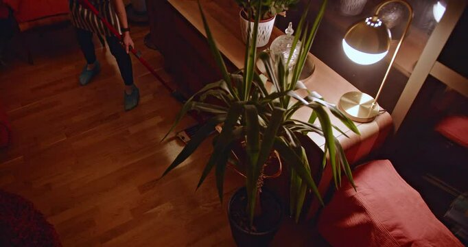 A person mops a hardwood floor in a cozy, dimly lit living room. The warm lighting creates a relaxing atmosphere.