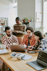 Vertical shot of biracial team of app developers sitting at table and looking at screen of laptop while having informal meeting