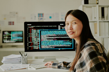 Portrait of attractive smiling young programmer sitting at her work desk with huge monitor...