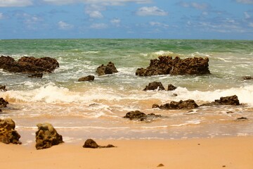 Green water sea, waves breaking at water edge, dark reef rocks. Tropical beach of Tabatinga near Joao Pessoa, Paraiba state, Brazil northeast. Touristic place for vacation travel.