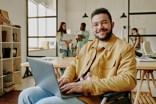 Portrait of handsome and confident developer smiling at camera while typing on keyboard of laptop