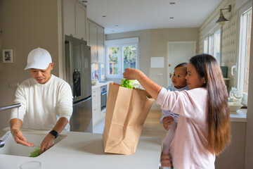 Young family unpacking groceries together in modern kitchen