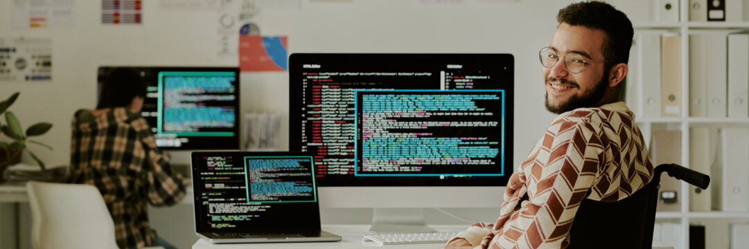Website banner with young programmer smiling at camera while posing for portrait with computers in background