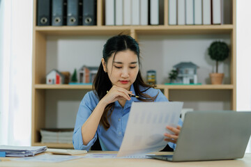 An Asian woman employee focused on completing the monthly sales summary with dedication.