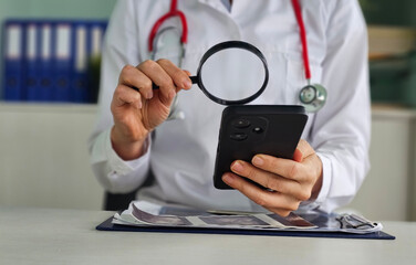 Doctor examining medical records on smartphone using magnifying glass in hospital