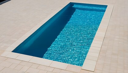 a rectangular swimming pool with shimmering blue water is surrounded by light beige brick paving.