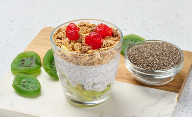 Yogurt and chia seed pudding in a glass, kiwi pieces. White table
