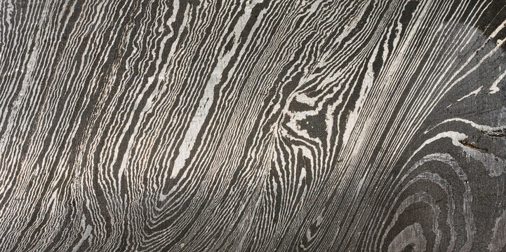 Detailed close up of damascus steel, showcasing its characteristic wavy and layered pattern of light and dark metal.
