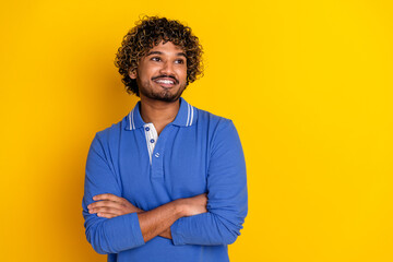 Smiling young man with curly hair wearing a blue polo shirt against a vibrant yellow background,...