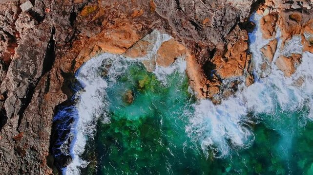 Turquoise waves crashing against rocky maltese coastline in dynamic aerial sequence