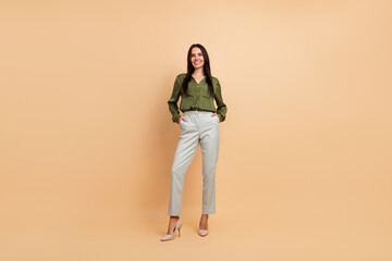 Confident businesswoman in a stylish green blouse and beige pants posing against a beige studio...