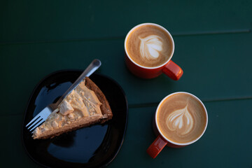 Two ceramic cups filled with rich latte coffee and a delicious piece of cake on a table in a cozy cafe. A perfect setting for enjoying a relaxing break or casual meeting with friends