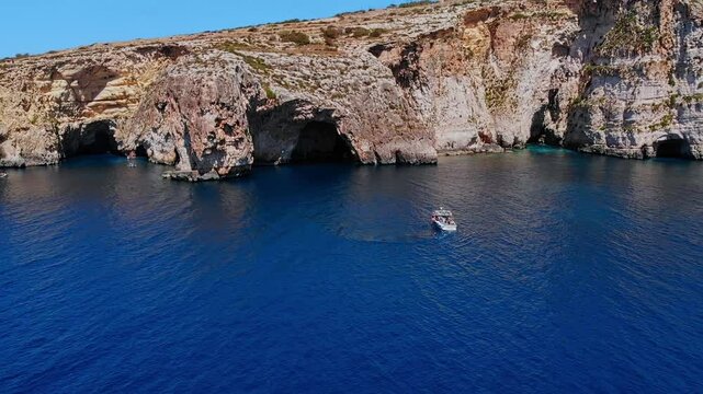 Aerial top view Blue Grotto in Malta. Pleasure boat with tourists runs. Natural arch window in rock