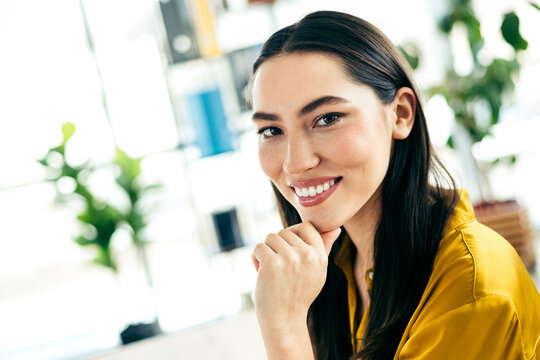 Young professional woman in modern office wearing stylish yellow shirt, smiling confidently, with green plants