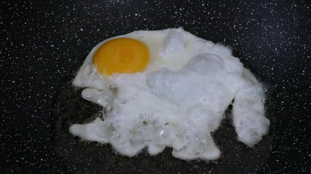 Cooking fried eggs sunny side up with a sizzling oil in frying pan.