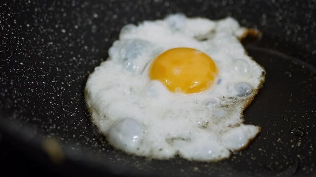 Cooking fried eggs sunny side up with a sizzling oil in frying pan.