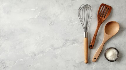A collection of cooking utensils like a metal whisk, tongs, and wooden spatula placed on a countertop with ample space for text