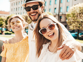 Group of young three stylish friends posing in the street. Fashion man and two cute female dressed...