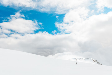 Lone hiker crossing a bright snowfield under vibrant blue sky and clouds in Sierra de Gredos, Spain, showcasing minimalism and solitude in a high-altitude alpine landscape