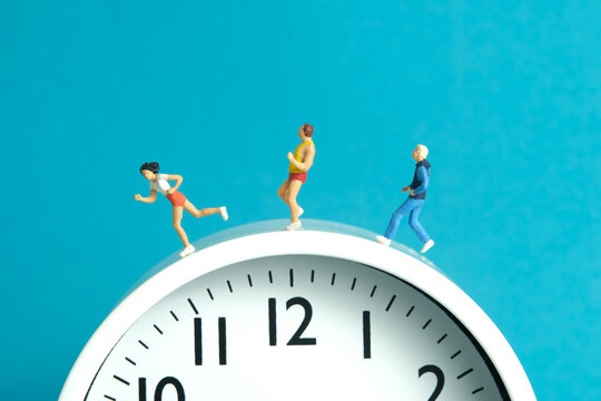 Miniature people toy figure photography. Running daily routine concept. A team group runner jogging above clock, isolated on blue background