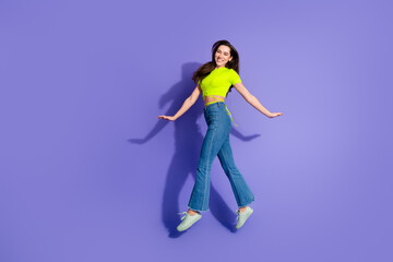 Smiling young woman in casual attire jumps against a vibrant purple background expressing joy and fun