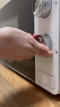 Close-up of a microwave oven in a modern kitchen as a young woman places food inside to heat. Everyday cooking routine. Ideal for home, kitchen appliance, or lifestyle themed videos.