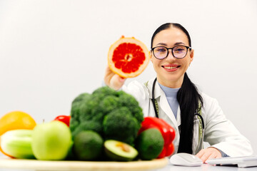 A nutritionist at a table with fruit, holding a grapefruit in a modern clinic office. The concept...