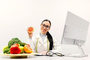 A nutritionist at a table with fruit, holding a grapefruit in a modern clinic office. The concept...