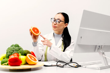 A nutritionist at a table with fruit, holding a grapefruit in a modern clinic office. The concept...