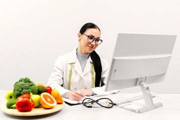 A young nutritionist works at a computer, creating a balanced corrective diet plan, with organic...