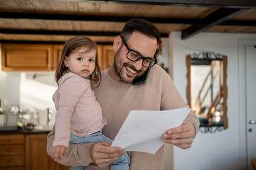 Father managing work and family, holding daughter and reading documents while on phone call
