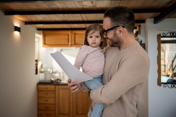 Father reading documents with daughter in his arms at home