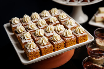 Tray of moist carrot cake squares topped with cream frosting, delicately dusted with powdered sugar