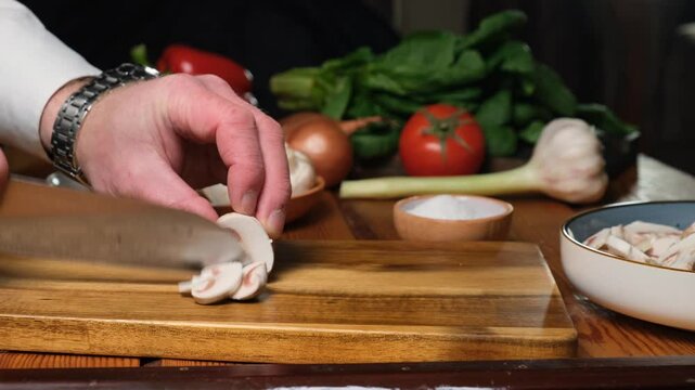 Chef's hand using knife and cutting board to cut fresh champignon mushrooms to cook vegetable, mushroom and cheese stew. Vegetarian food. Diet and healthy eating.
